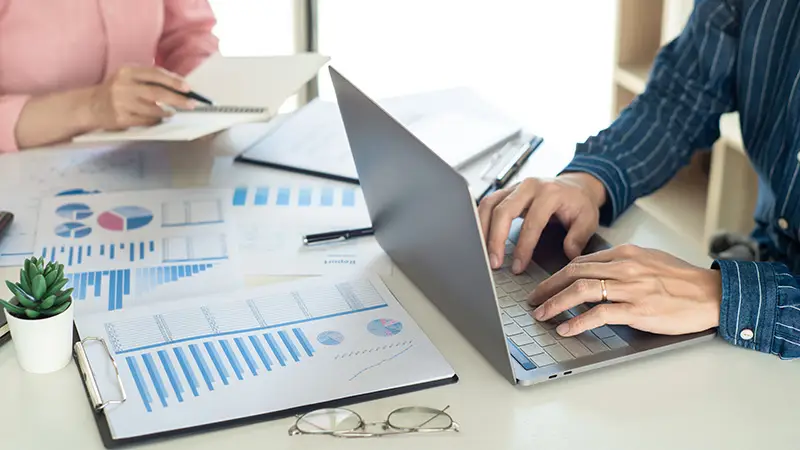 Close up of a man's hand using a laptop while reviewing financial documents